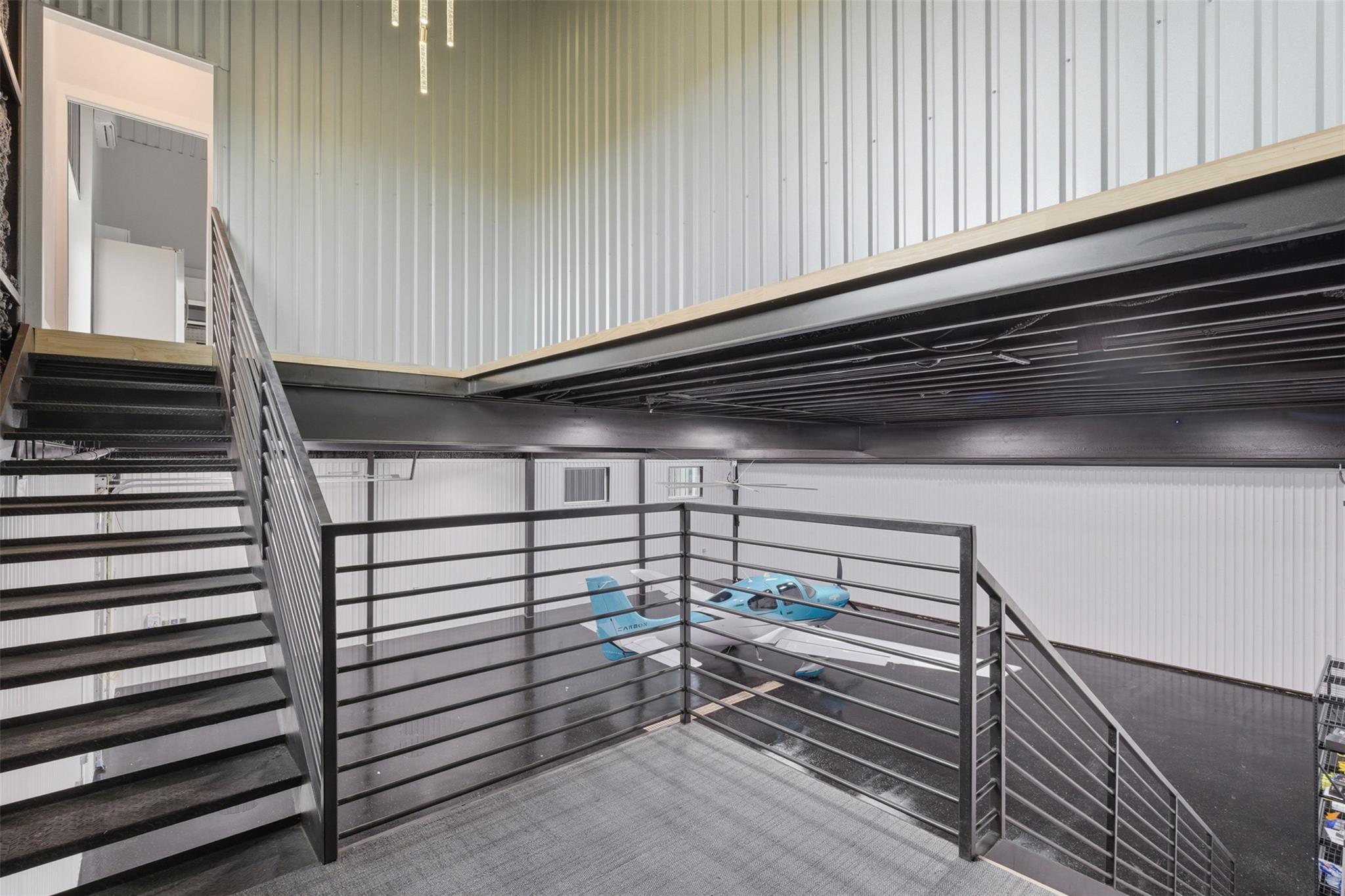 Aircraft hangar mezzanine overlooking a blue-and-white airplane, with black metal stairs and railings.