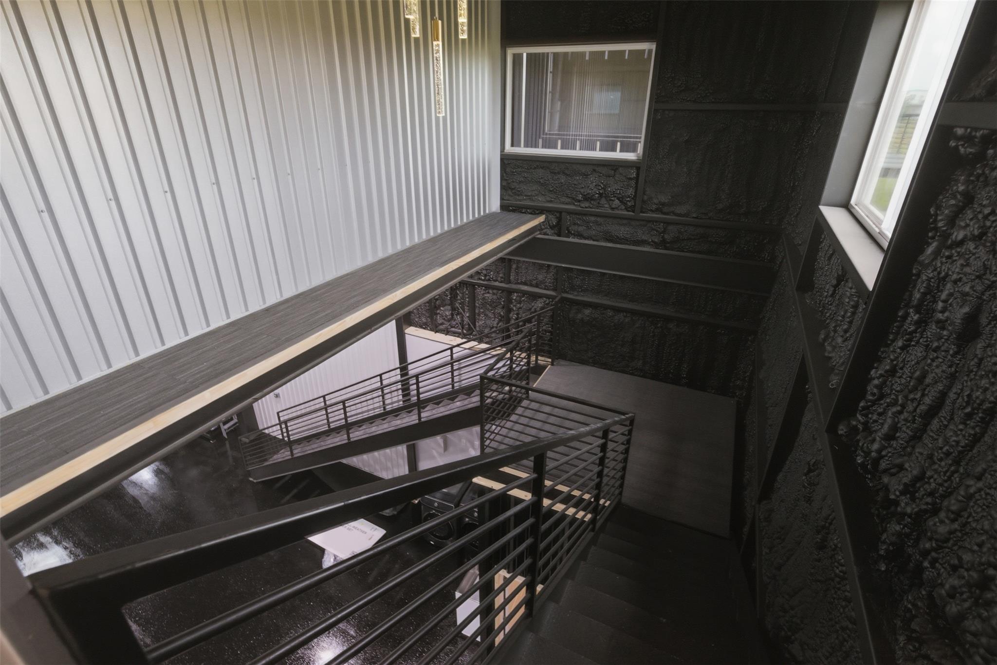 Industrial stairwell with black metal railings, dark textured walls, and a white corrugated wall.