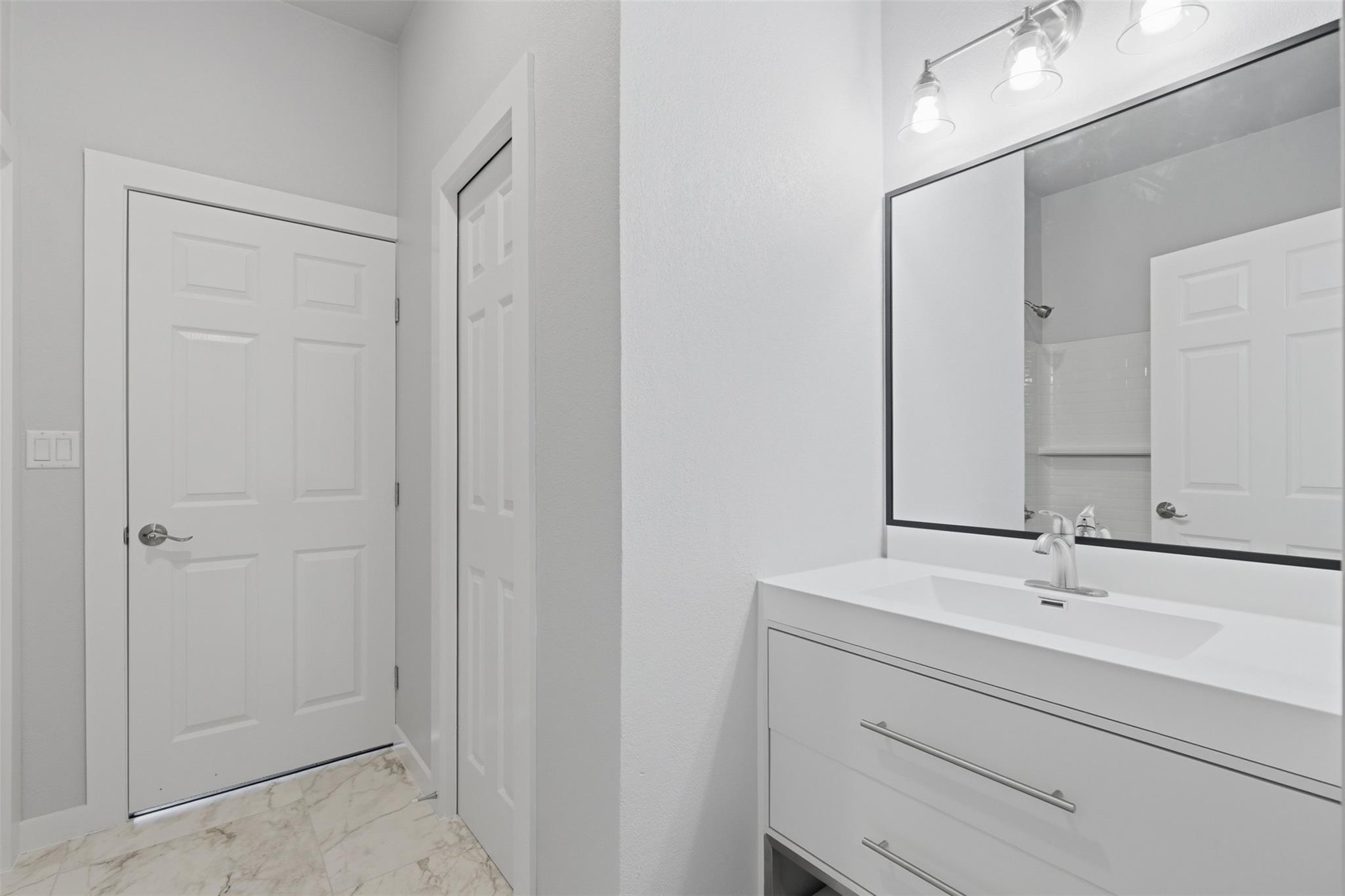 Bathroom with a white vanity, large mirror, paneled doors, and marble-look floor.