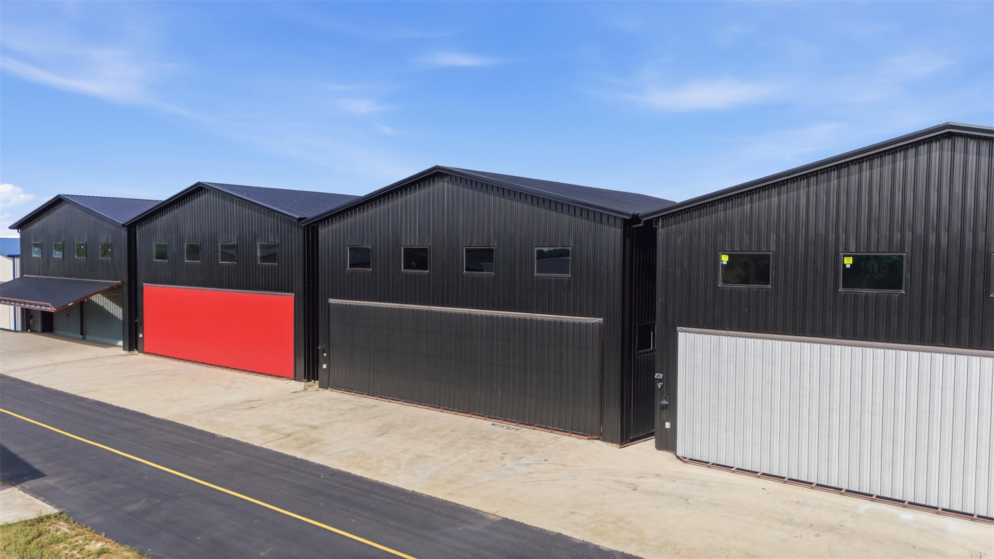 Commercial warehouse units with dark metal siding and a bright red roll-up door beside a paved drive.