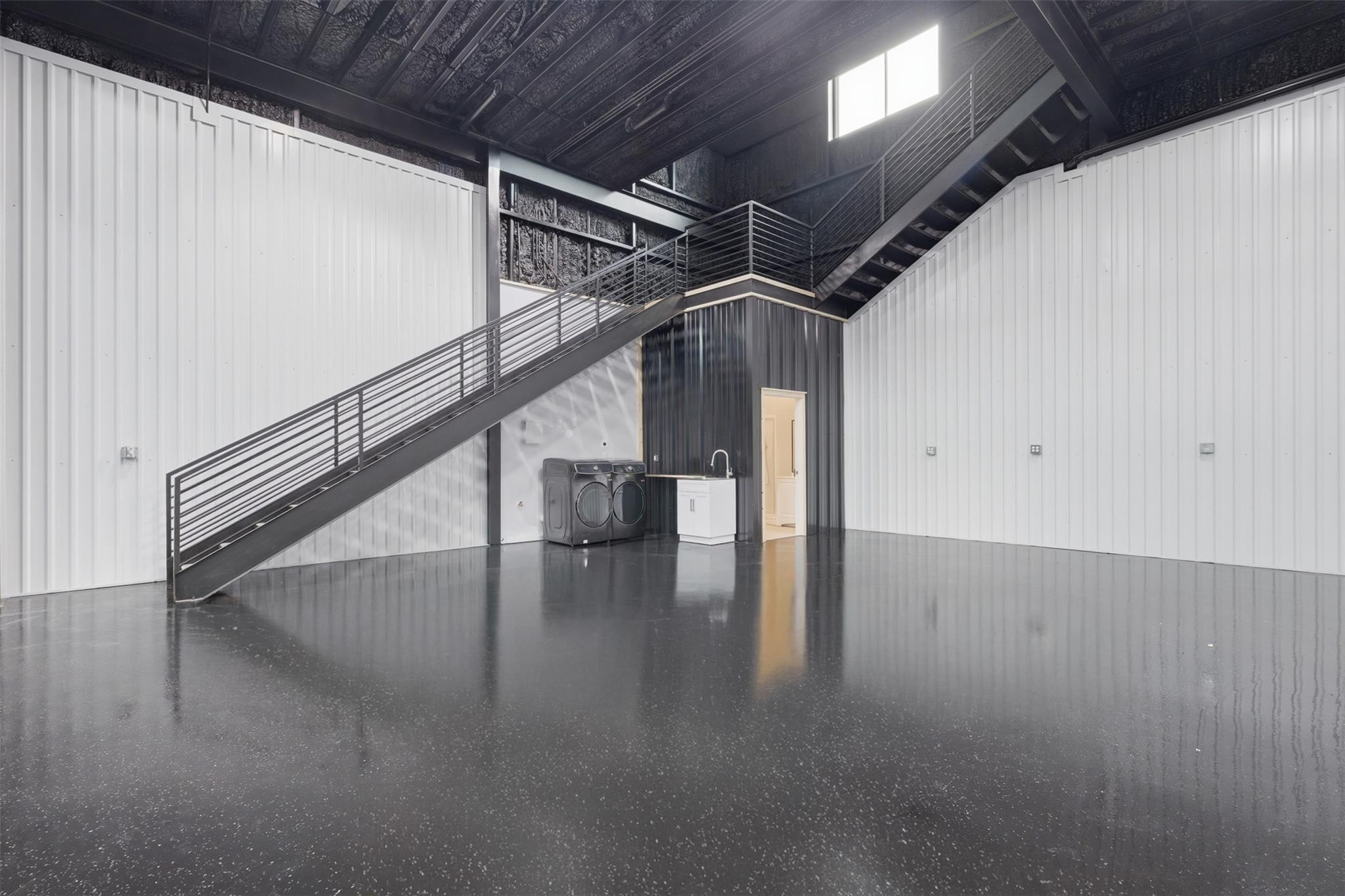 Industrial interior with a staircase to a mezzanine, polished floor, and laundry appliances.