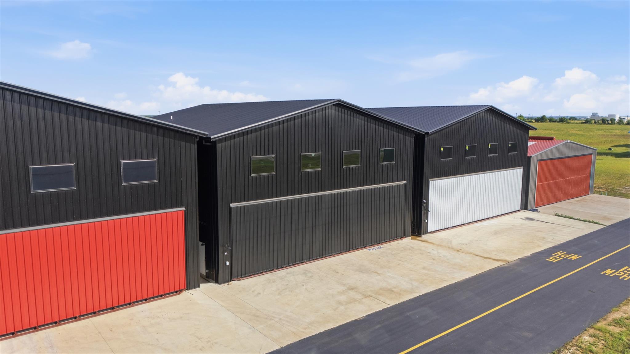 Aerial view of metal hangars with red and white doors along a paved lane.