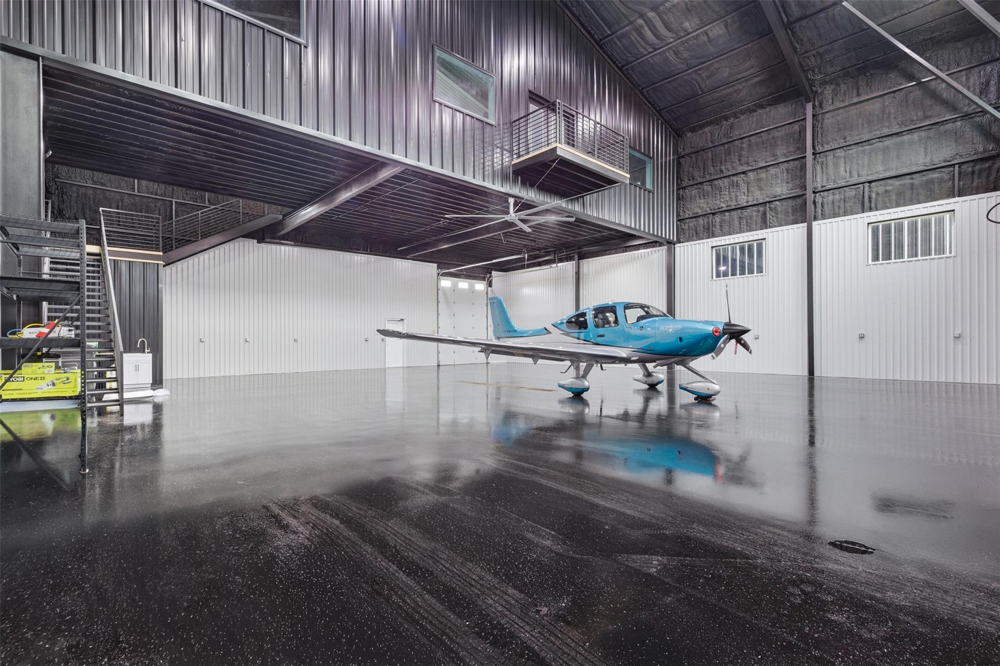 Blue airplane inside a spacious hangar with a mezzanine and polished concrete floor.