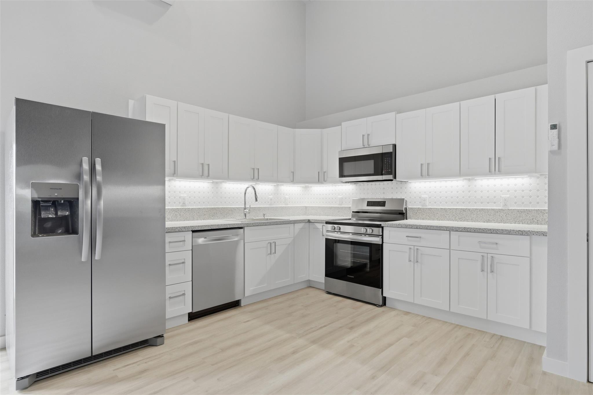 Vacant kitchen with white cabinets, stainless steel appliances, and pale wood floors.
