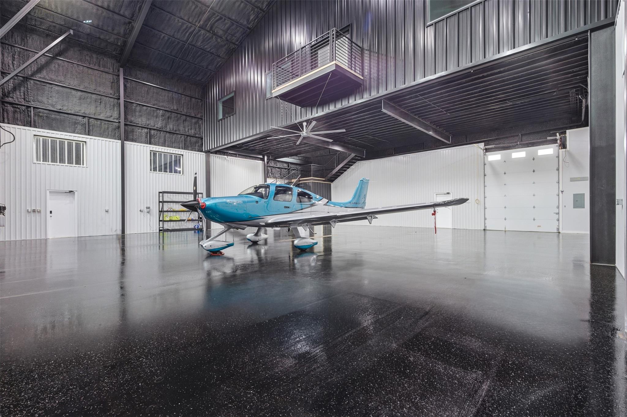 Aircraft hangar with a blue-and-white plane, mezzanine, and polished floor.