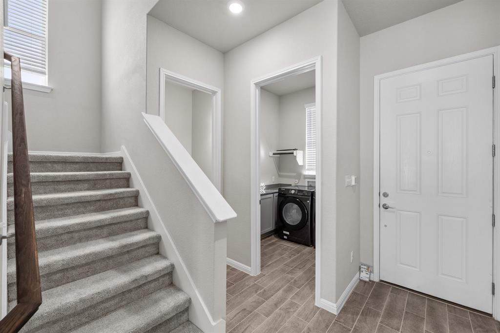Entryway with carpeted stairs, white front door, and washer and dryer in the adjacent laundry area.