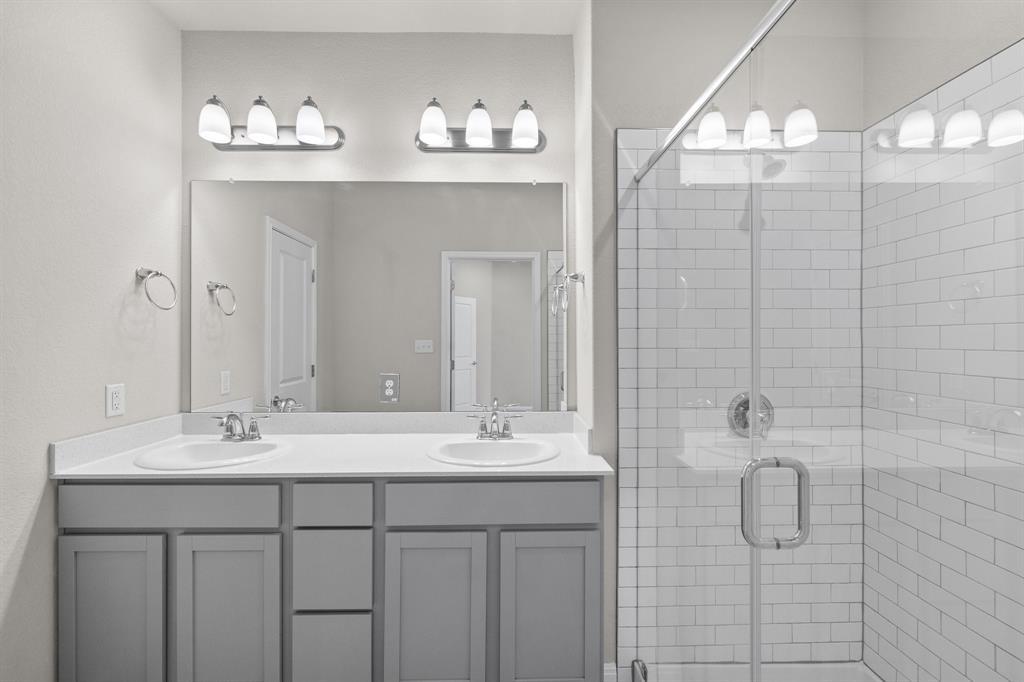 Bathroom with a double-sink vanity and a glass shower lined with white subway tile.