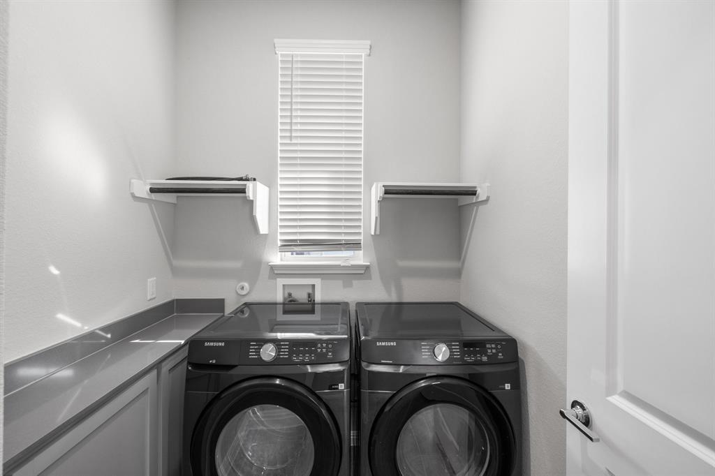 Laundry room with black Samsung washer and dryer, gray countertop, and window with white blinds.