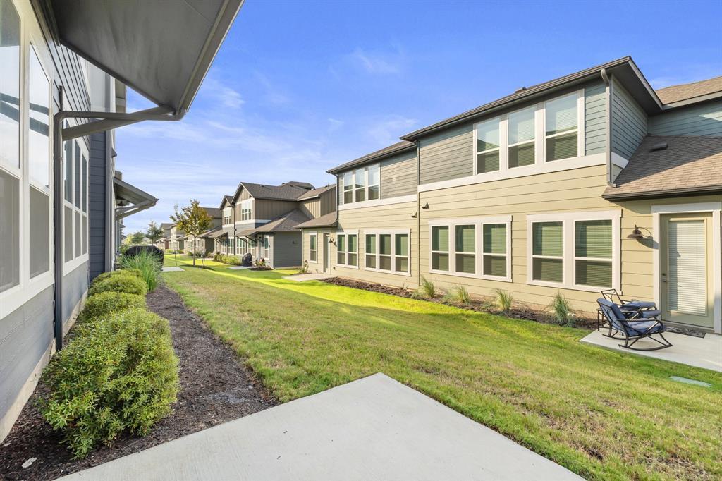 Attached homes surround a grassy courtyard with a concrete patio and outdoor chairs.