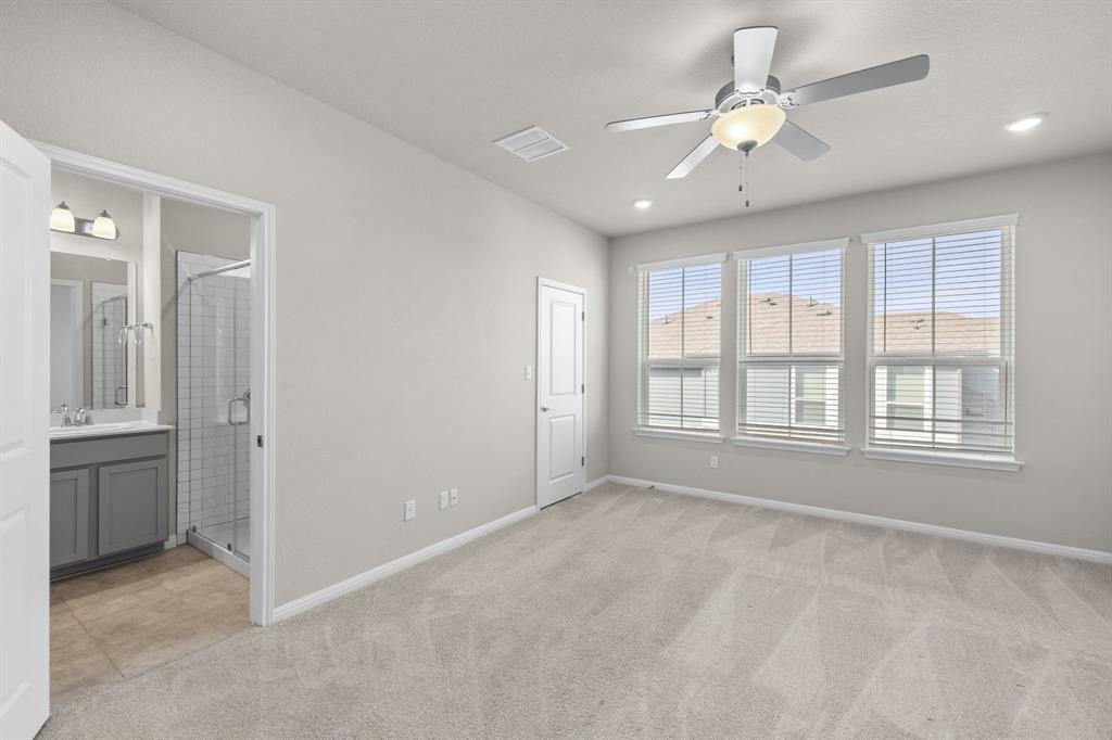 Empty carpeted bedroom with a ceiling fan, three windows, and an adjoining bathroom.