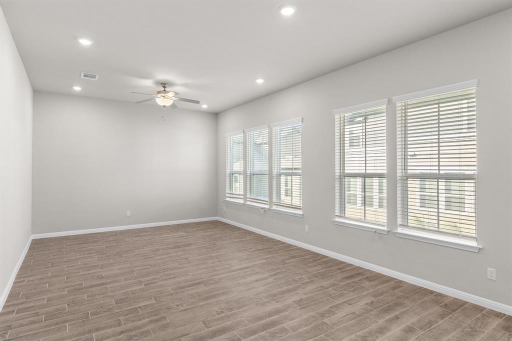 Empty room with wood-look tile flooring, multiple windows with blinds, and a ceiling fan.