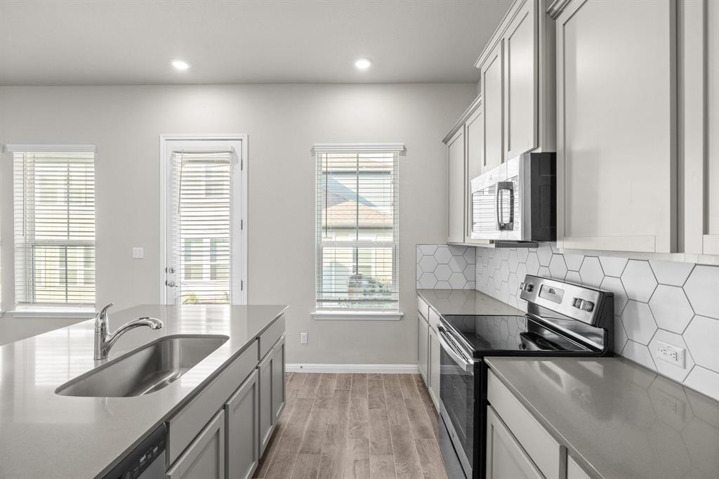 Kitchen with a gray island, stainless steel appliances, and white hexagonal tile backsplash