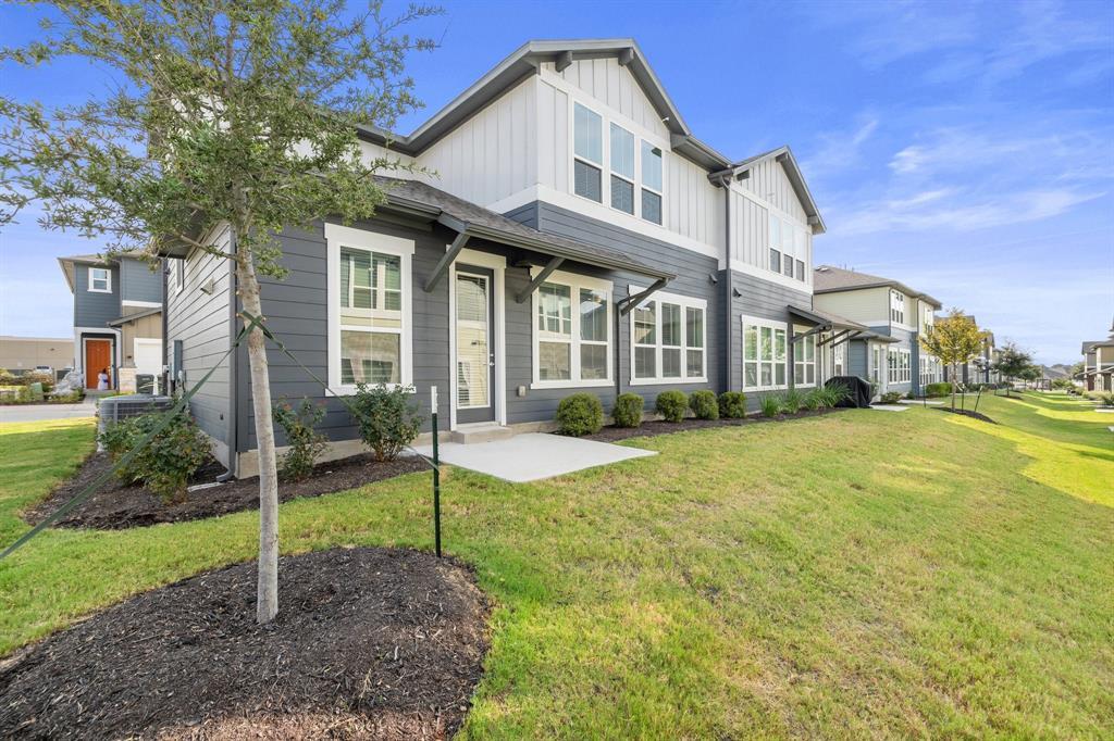 Modern gray two-story townhome with white upper siding, large windows, and a landscaped lawn.