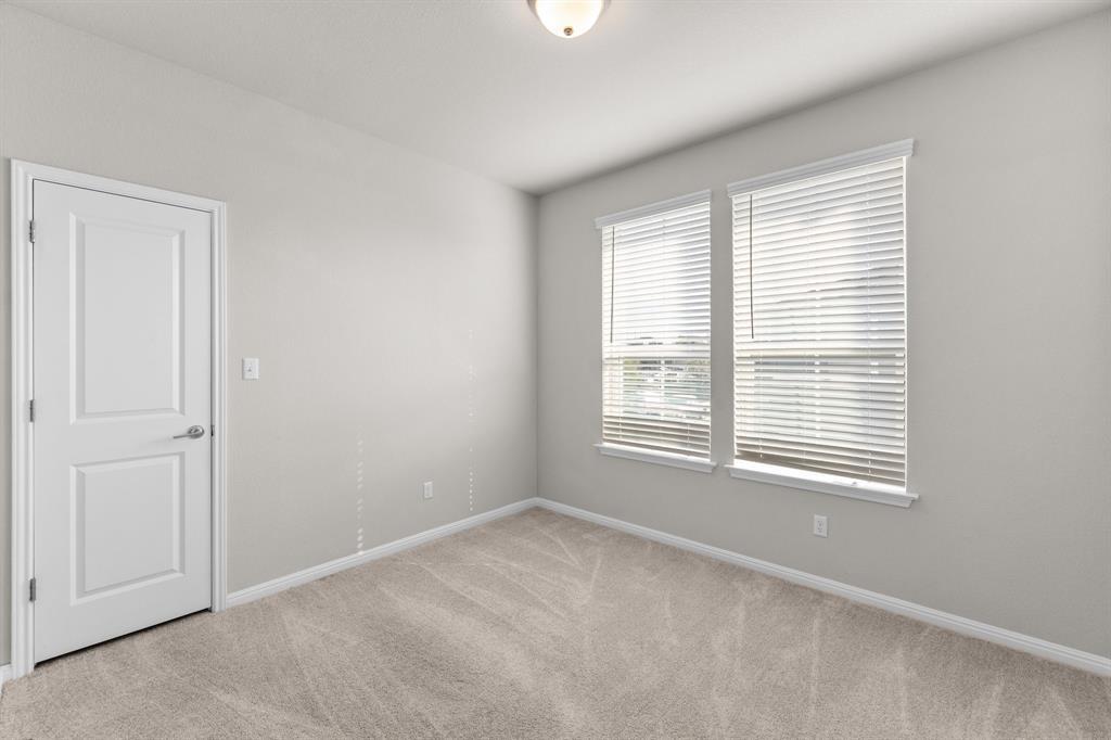 Empty carpeted room with a white paneled door and two windows with blinds.