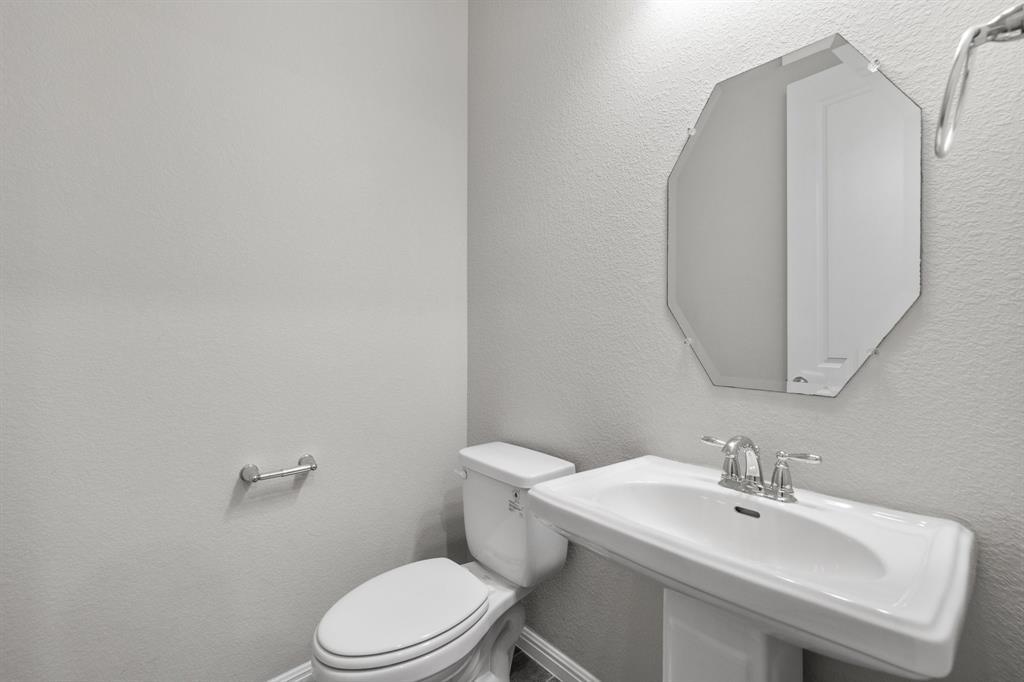 Vacant bathroom with a white toilet, pedestal sink, chrome fixtures, and octagonal mirror.