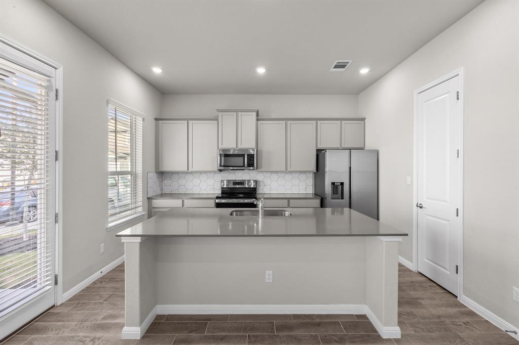 Unfurnished kitchen with a large island, gray cabinets, stainless steel appliances, and geometric tile backsplash.