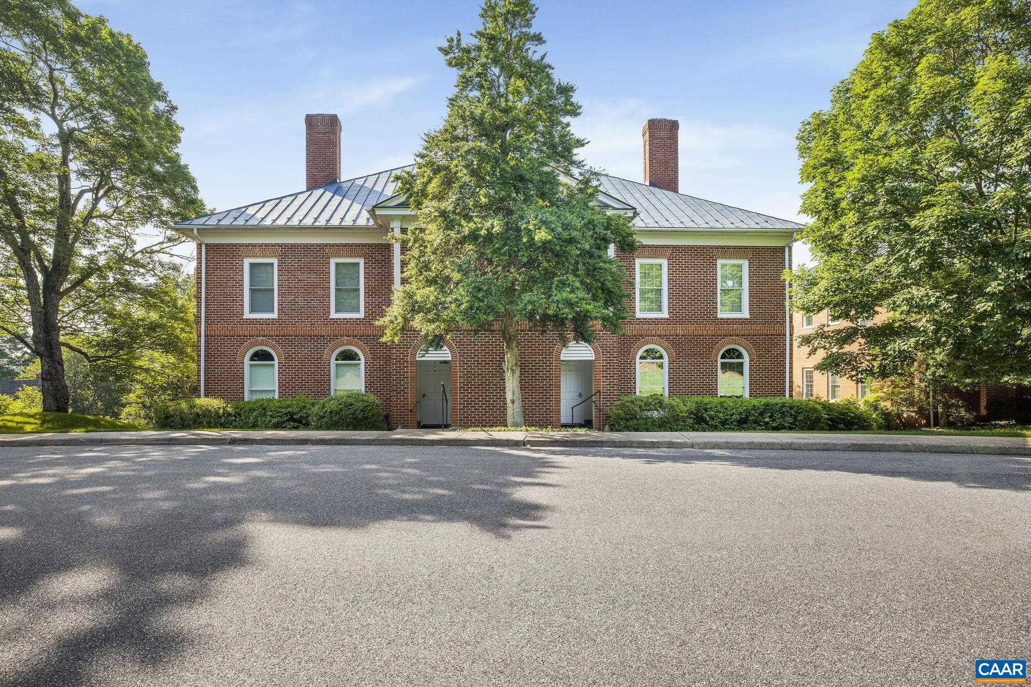 Two-story brick building with paired arched entrances, a metal roof, and mature trees.