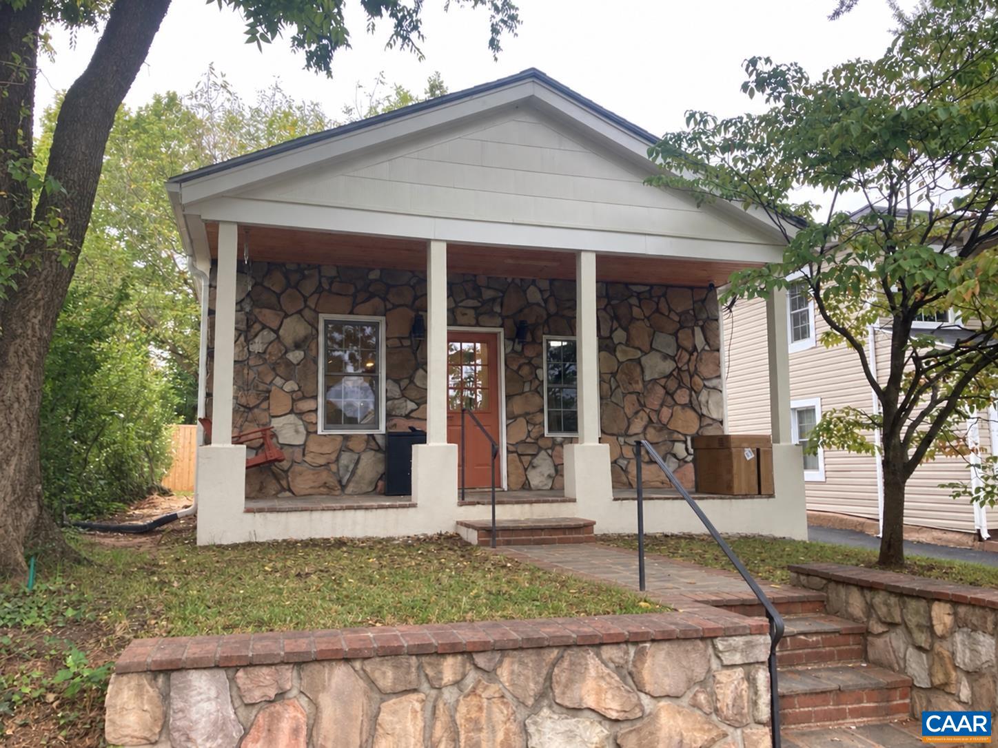 Stone-front house with a covered porch, red door, and brick steps.