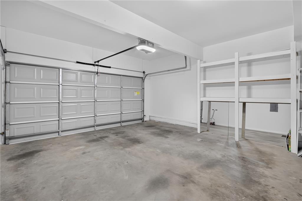 Empty garage with a wide paneled door, overhead opener, and wall-mounted storage shelves.