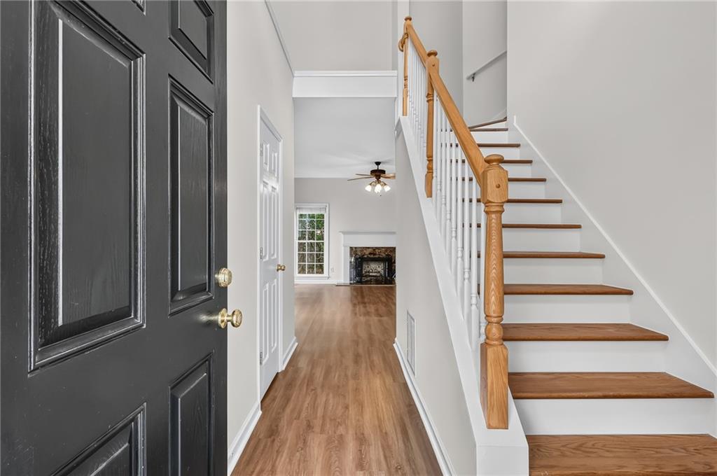 Entry foyer with a black paneled door, wood staircase, and hallway leading to a fireplace.