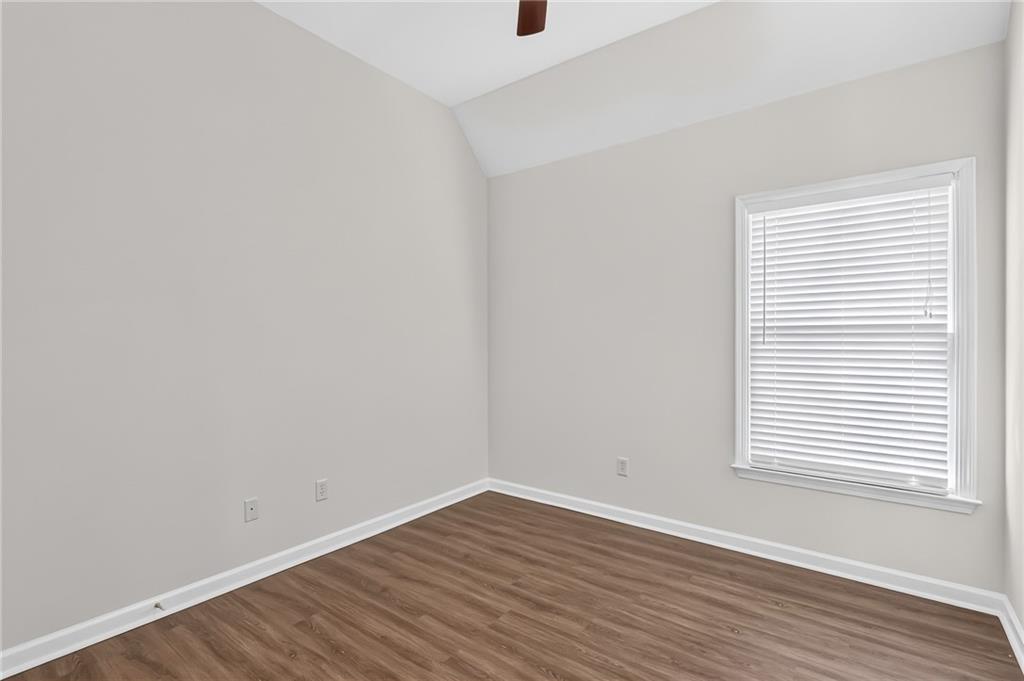 Empty room with brown wood-look flooring and a window with closed blinds.