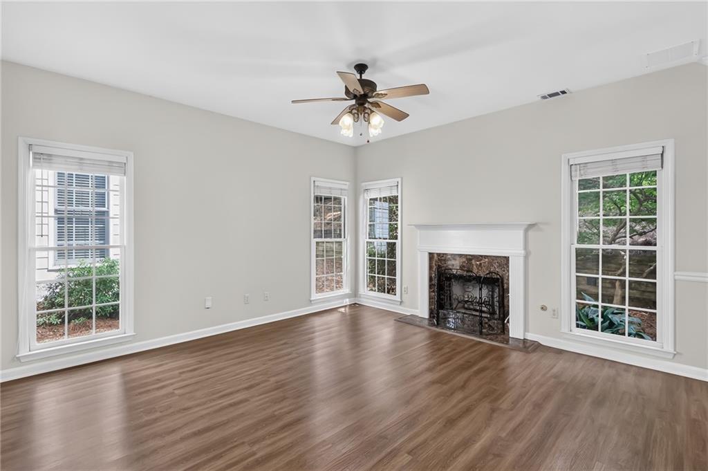 Empty living room with a white mantel fireplace, large windows, and wood-look flooring.
