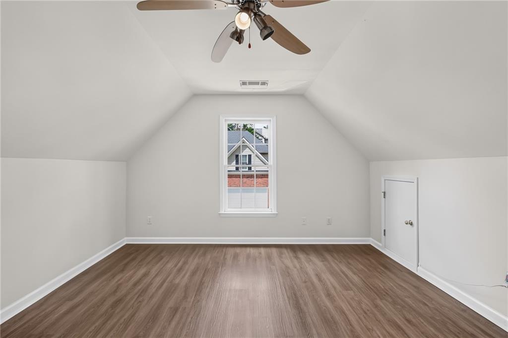 Vacant room with a vaulted ceiling, wood-look flooring, ceiling fan, and centered window.
