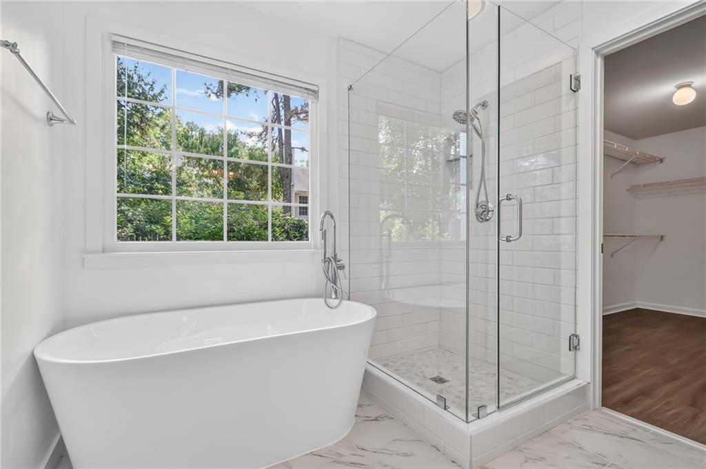 Bright bathroom with a freestanding tub, glass shower, and large window overlooking greenery.