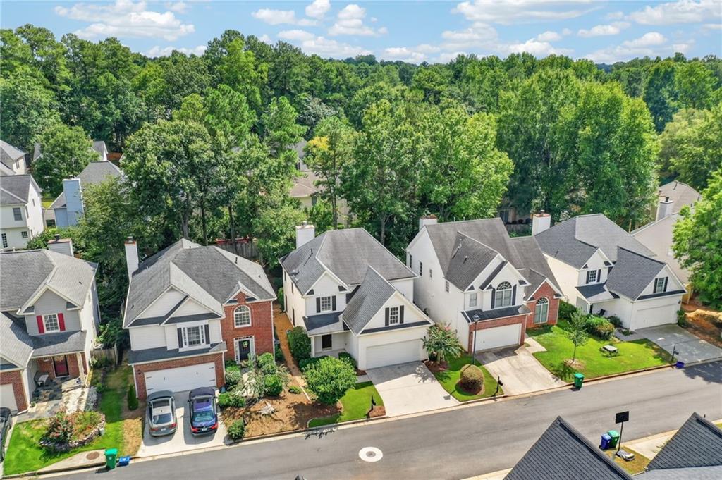 Aerial view of detached homes along a tree-lined street with front lawns and driveways.