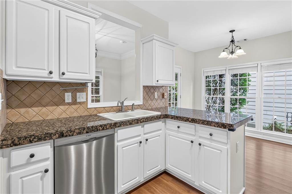 Kitchen with white cabinets, granite counters, stainless steel dishwasher, and large windows.