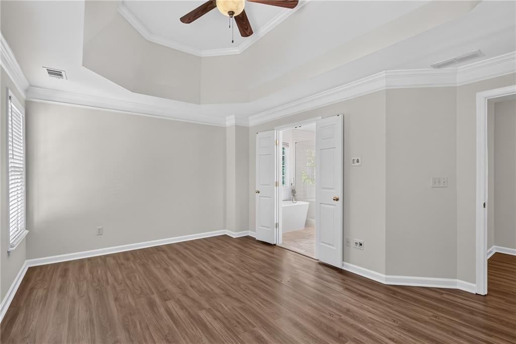 Empty bedroom with wood-look flooring, ceiling fan, and open doorway to an adjoining bathroom.
