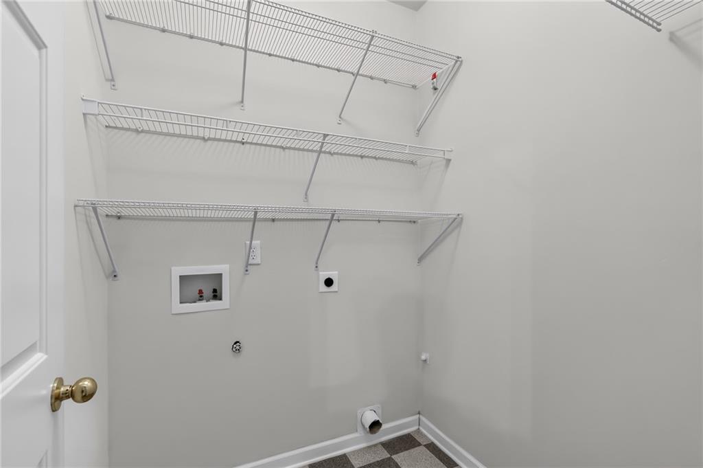 Empty laundry room with wire shelving, washer and dryer hookups, and gray tile flooring.