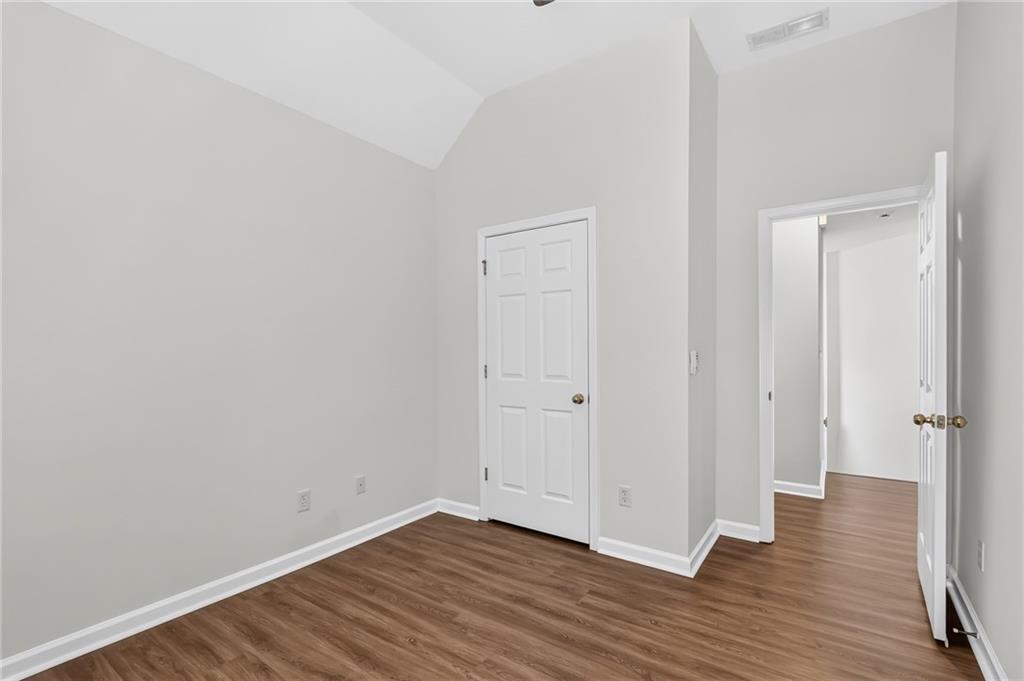 Empty room with vaulted ceiling, brown wood-look floors, and an open doorway to the hall.