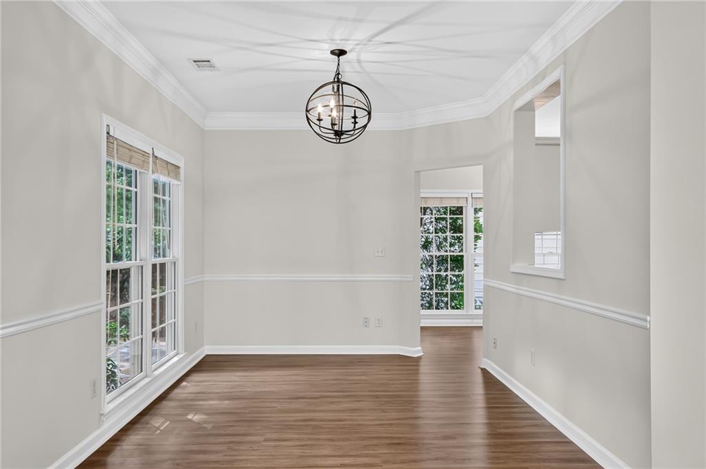 Empty dining room with hardwood floors, tall windows, and a dark metal chandelier.