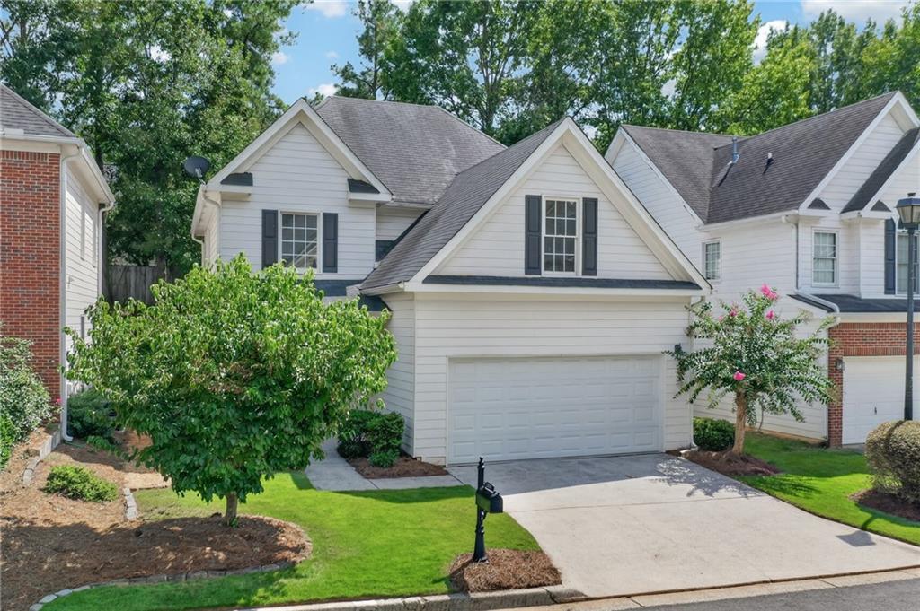 White two-story house with a double garage, gray roof, and flowering shrubs along the driveway.