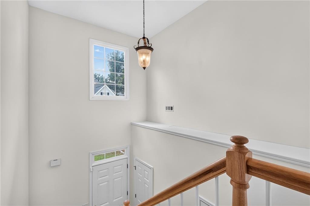 Upper stair landing overlooking the front entry, with a wooden railing and pendant light.