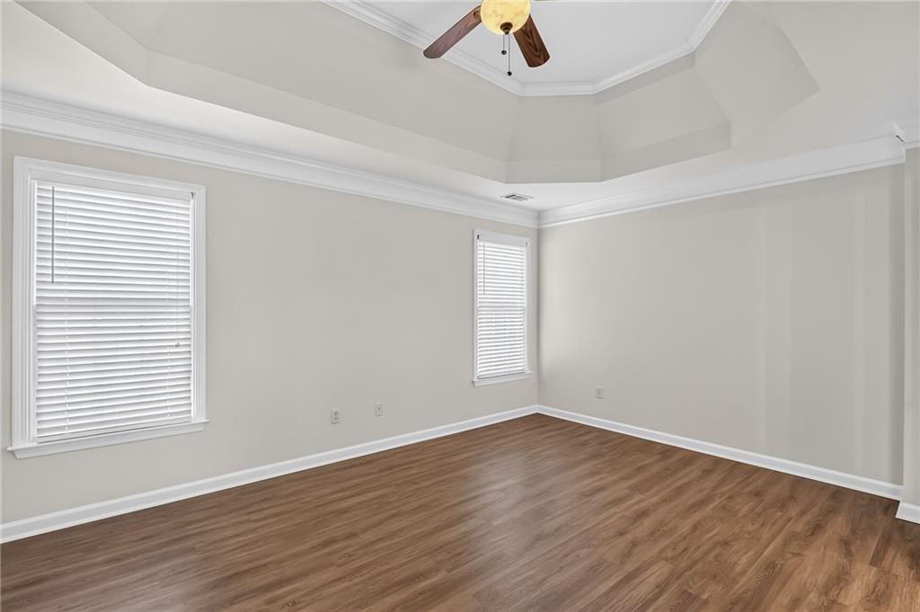 Empty room with wood-look flooring, two blinded windows, and a raised ceiling with a fan.