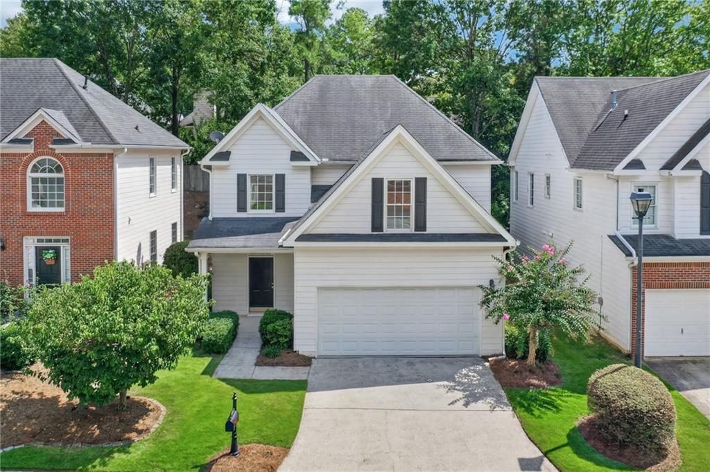 White two-story house with a double garage, landscaped lawn, and flowering shrubs.