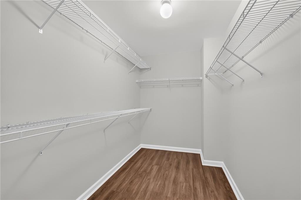 Walk-in closet with white wire shelving and brown wood-look flooring.