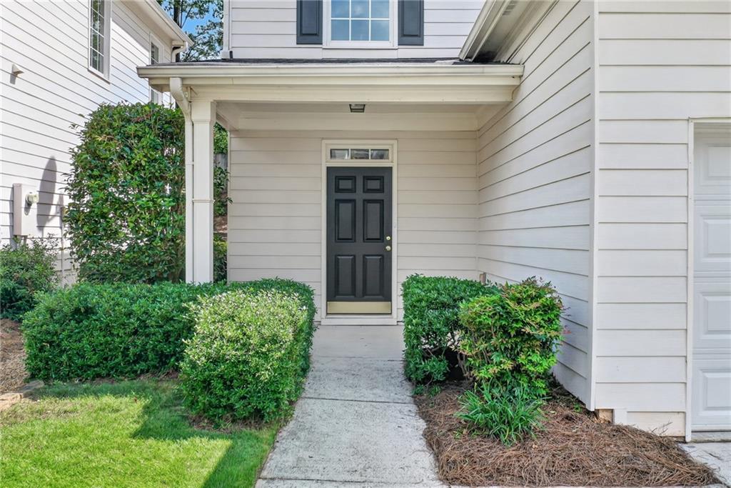 House entrance with a covered porch, black paneled door, and hedges along the walkway.