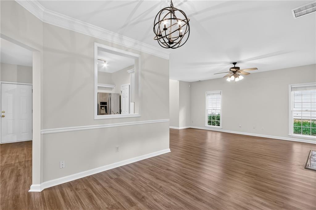 Unfurnished living and dining area with wood-look floors, a kitchen pass-through, and ceiling fan.