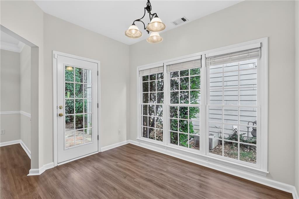Empty room with plank flooring, a glass-paned exterior door, large windows, and a three-light chandelier.