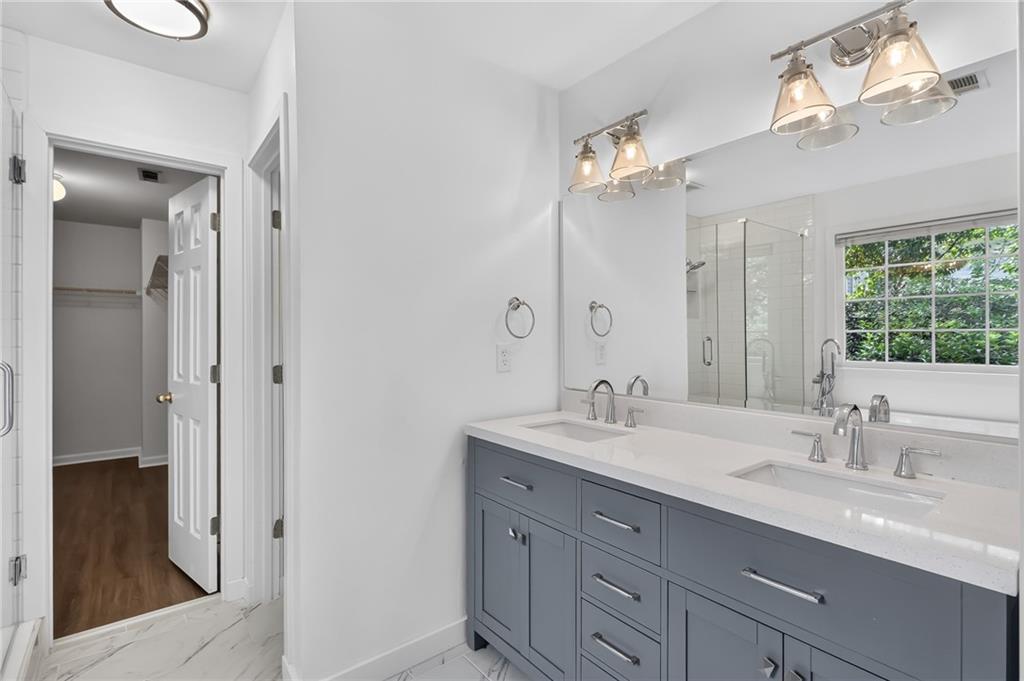 Bathroom with a blue-gray double vanity, large mirror, and glass shower beside a window.