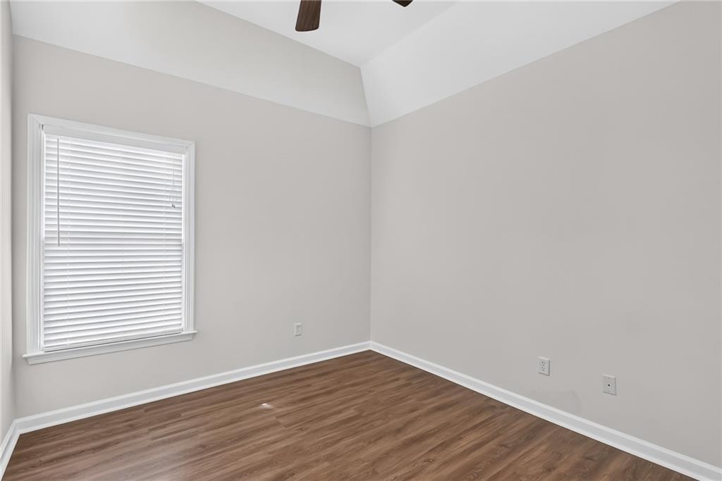Empty bedroom with wood-look flooring, a window with white blinds, and a vaulted ceiling.