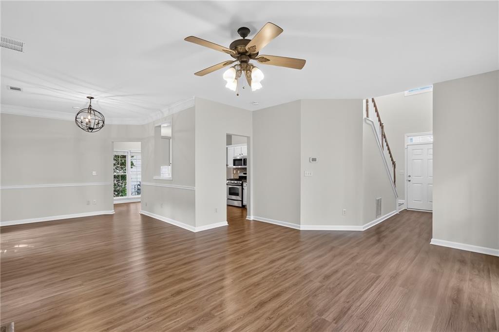 Vacant open-plan living and dining area with wood-look floors, ceiling fan, kitchen opening, and staircase.