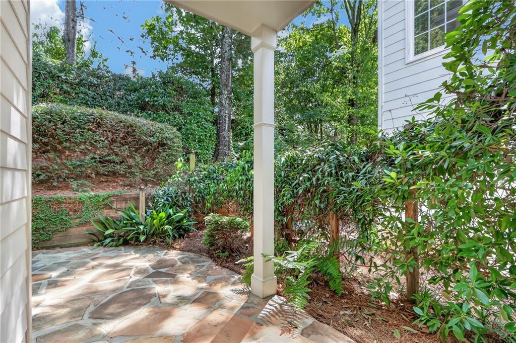Covered stone patio with a white support column and dense surrounding greenery.