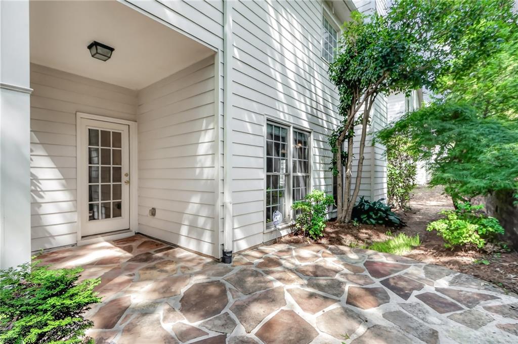 House side entrance with a glass-paneled door and irregular stone patio beneath mature trees.