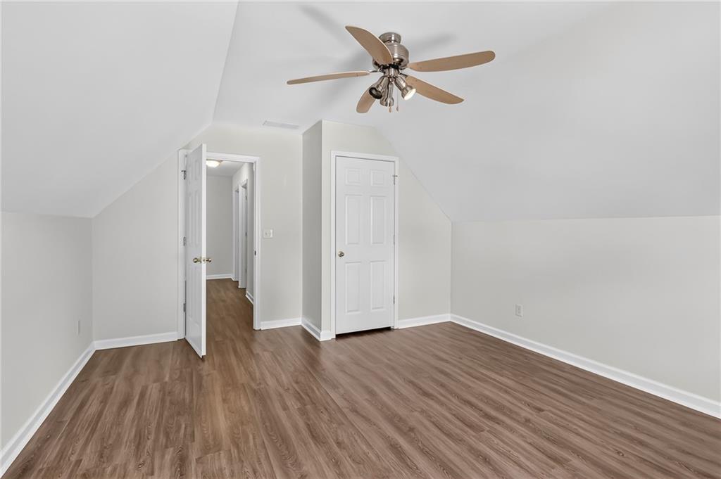 Empty bedroom with wood-look flooring, sloped ceilings, and a ceiling fan.
