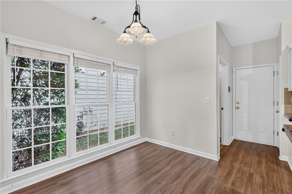 Unfurnished dining area with large windows, a three-light chandelier, and wood-look flooring.