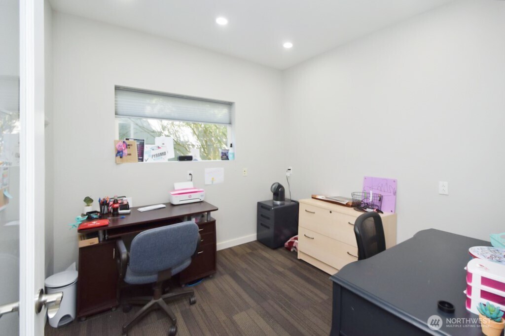 Furnished office with two desks, a filing cabinet, and a window with a partially lowered blind.